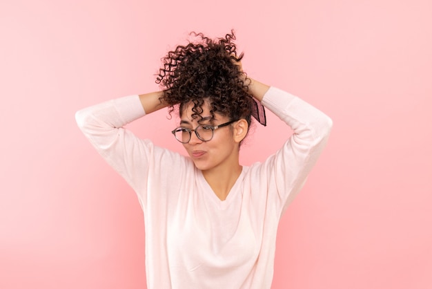 Vista frontal de la joven jugando con su cabello en la pared rosa