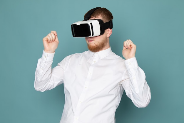 Una vista frontal joven jugando vr en camiseta blanca en el espacio azul