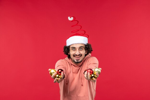 Foto gratuita vista frontal del joven con juguetes del árbol de navidad en la pared roja