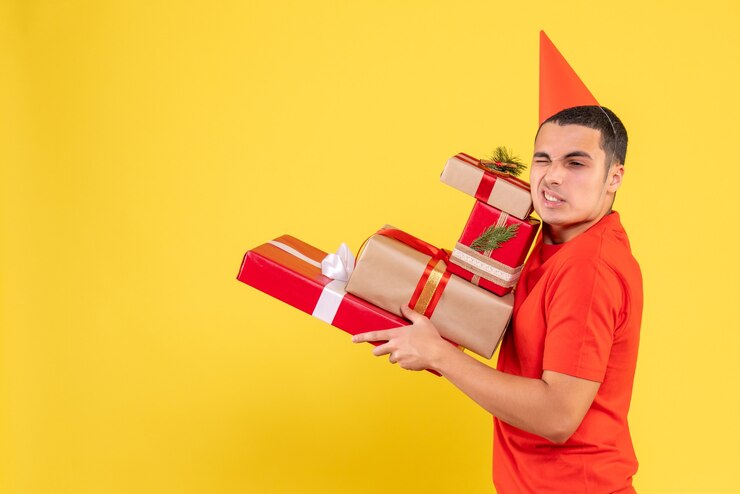 Foto gratuito vista frontal del joven llevando regalos de navidad en la pared amarilla