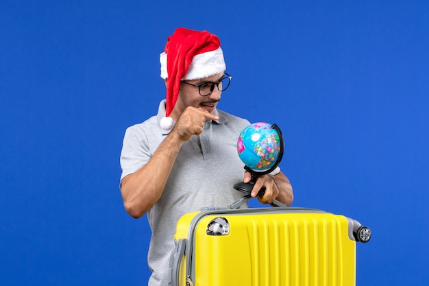 Vista frontal joven macho con bolsa amarilla con globo en la pared azul viaje de vacaciones en avión