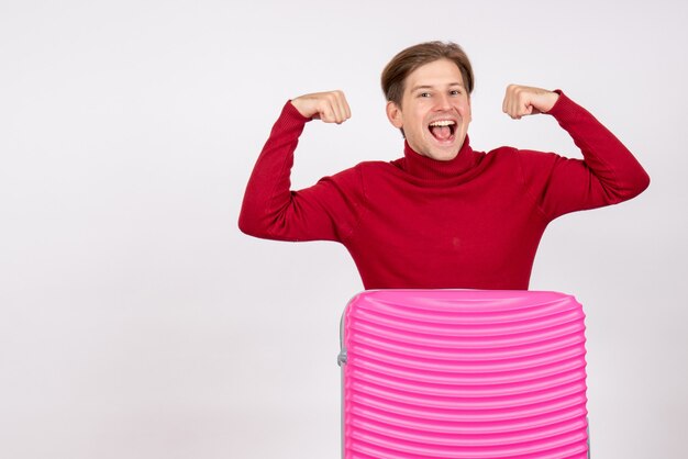 Vista frontal del joven macho con bolsa rosa flexionando sobre pared blanca