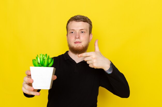 Vista frontal del joven macho en camisa negra con pequeña planta verde