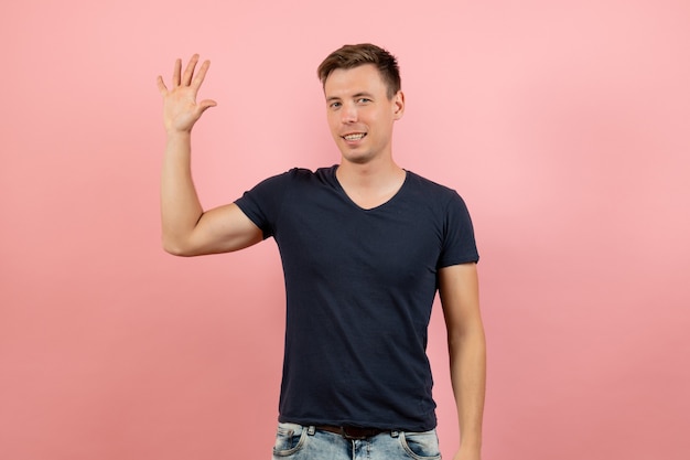 Vista frontal joven macho en camiseta azul mostrando su palma sobre fondo rosa modelo de color de emoción humana masculina