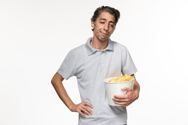Vista frontal joven macho comiendo papas fritas mientras ve una película destacó en la superficie blanca