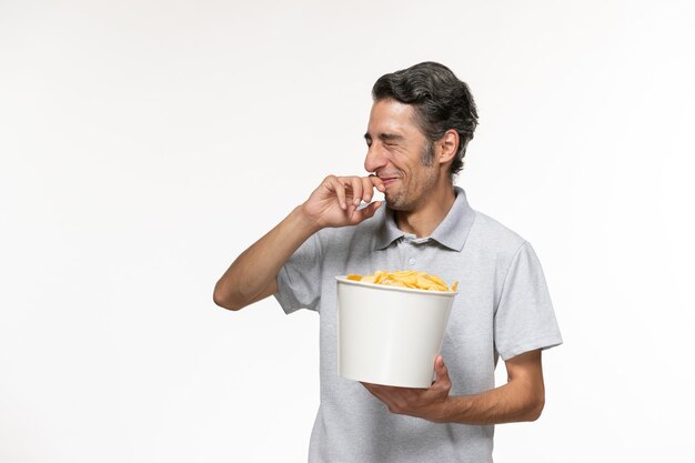 Vista frontal joven macho comiendo papas fritas con risas sobre superficie blanca