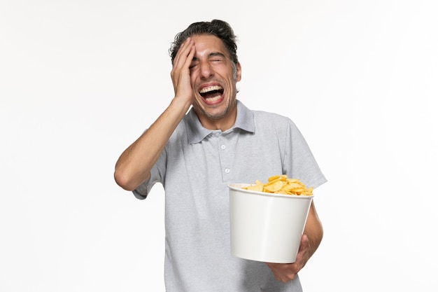 Vista frontal joven macho comiendo papas fritas sobre superficie blanca