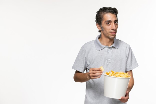 Vista frontal joven macho comiendo papas fritas sobre superficie blanca