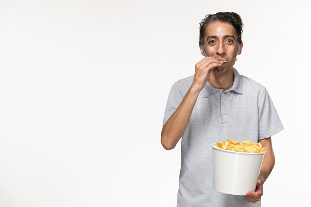 Vista frontal joven macho comiendo papas fritas sobre superficie blanca