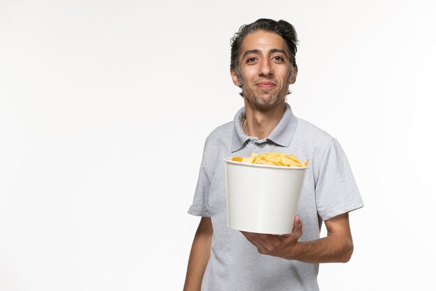 Vista frontal joven macho comiendo papas fritas sobre superficie blanca