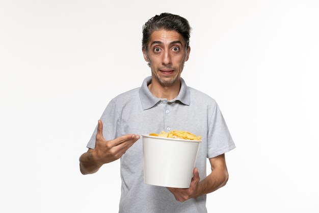 Vista frontal joven macho comiendo papas fritas sobre superficie blanca