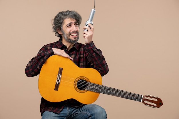 Vista frontal del joven macho con guitarra cantando en micrófono en la pared rosa