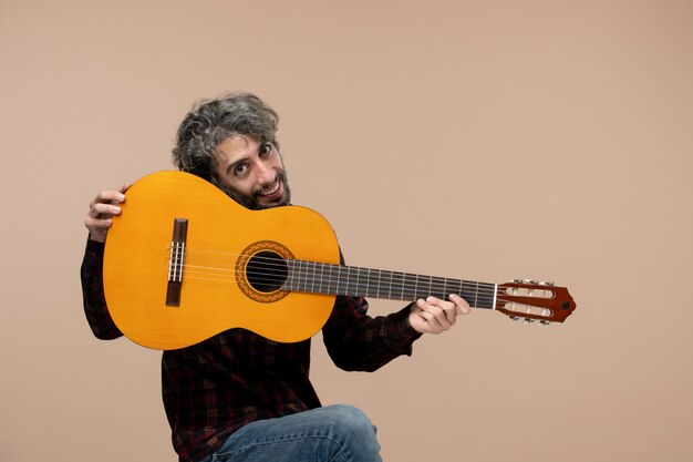 Vista frontal del joven macho con guitarra en la pared rosa