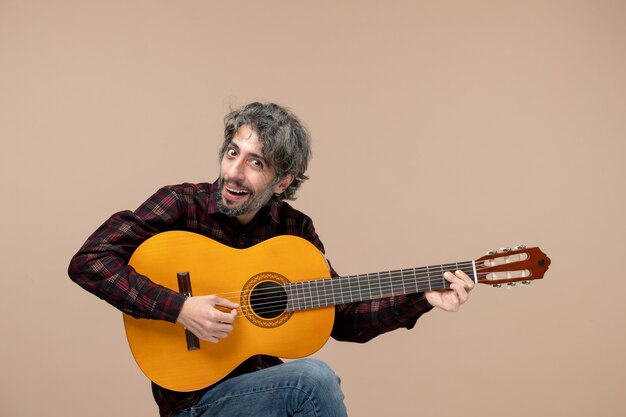 Vista frontal del joven macho con guitarra en la pared rosa