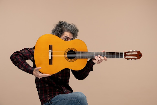 Vista frontal del joven macho con guitarra en la pared rosa