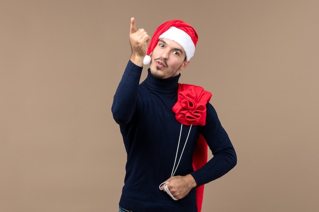 Vista frontal joven macho llevando presente bolsa sobre fondo marrón vacaciones de navidad santa