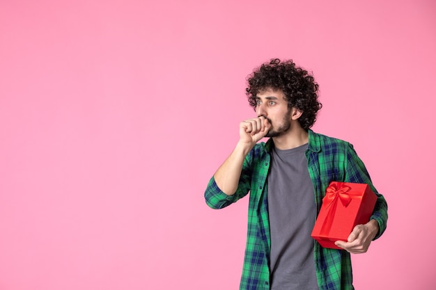 Foto gratuita vista frontal del joven macho con paquete rojo en la pared de color rosa claro