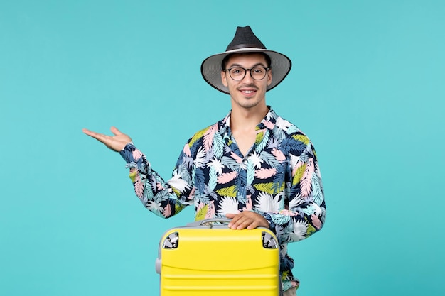 Vista frontal del joven macho con su bolsa amarilla preparándose para el viaje sobre una pared azul