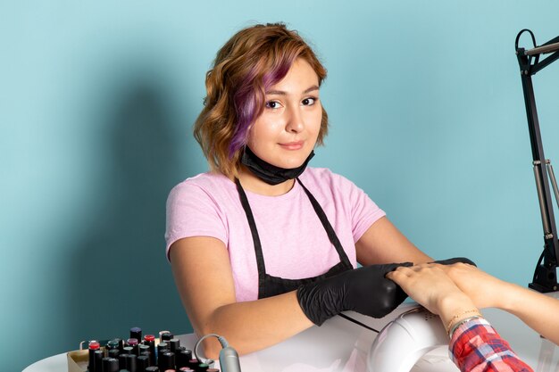 Una vista frontal joven manicura con guantes negros haciendo manicura en azul