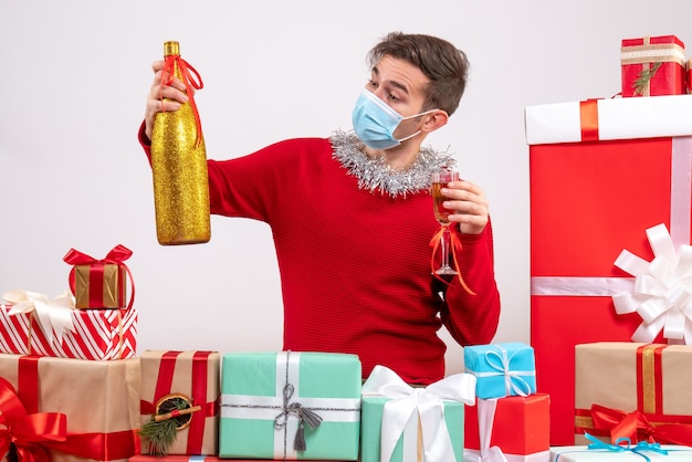 Vista frontal joven con máscara brindando sentados alrededor de regalos de Navidad