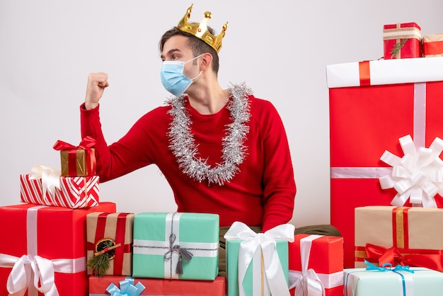 Vista frontal joven con máscara sentado en el piso regalos de Navidad