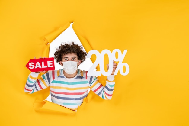 Vista frontal joven con máscara sosteniendo y venta escribiendo en color amarillo venta coronavirus salud covid- foto pandemia