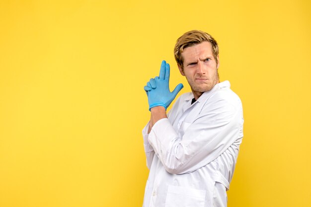 Vista frontal joven médico en arma sosteniendo pose sobre fondo amarillo medic covid pandemia