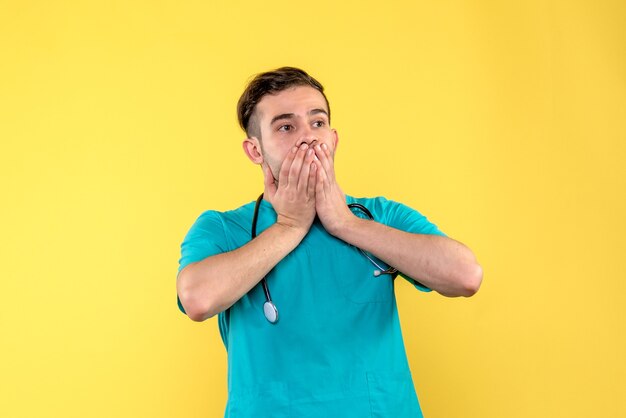 Vista frontal del joven médico conmocionado en la pared amarilla