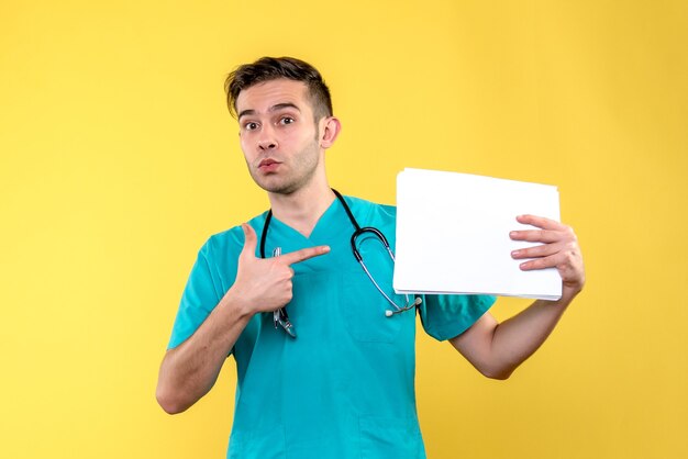 Vista frontal del joven médico con documentos en la pared amarilla