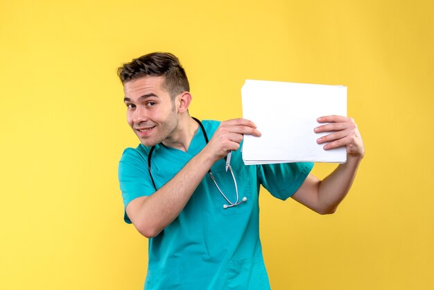Vista frontal del joven médico con documentos en la pared amarilla