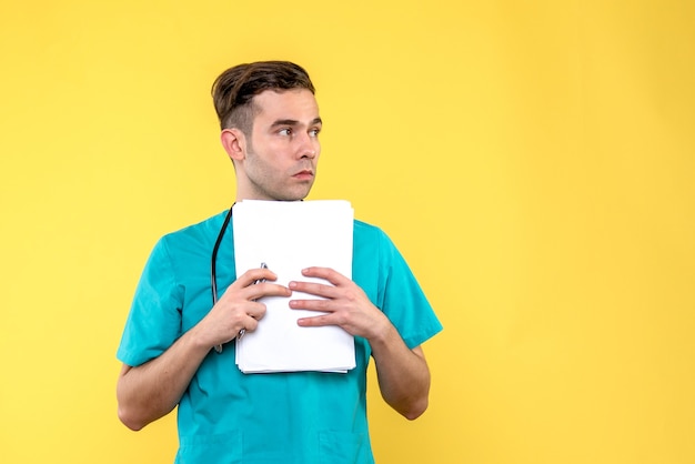 Vista frontal del joven médico con documentos en la pared de color amarillo claro