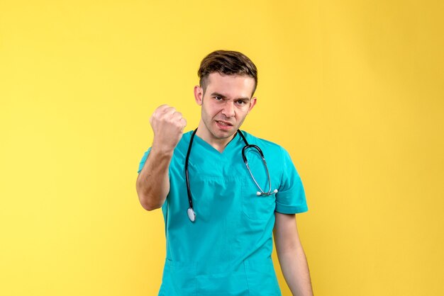 Vista frontal del joven médico que amenaza en la pared amarilla