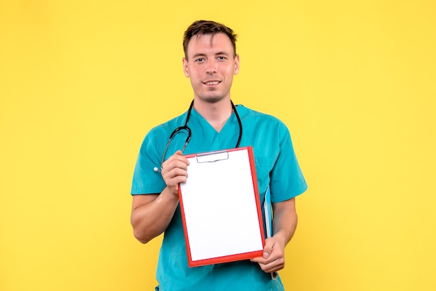 Vista frontal del joven médico sosteniendo análisis sobre pared amarilla