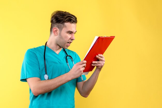 Vista frontal del joven médico sosteniendo análisis sobre pared amarilla