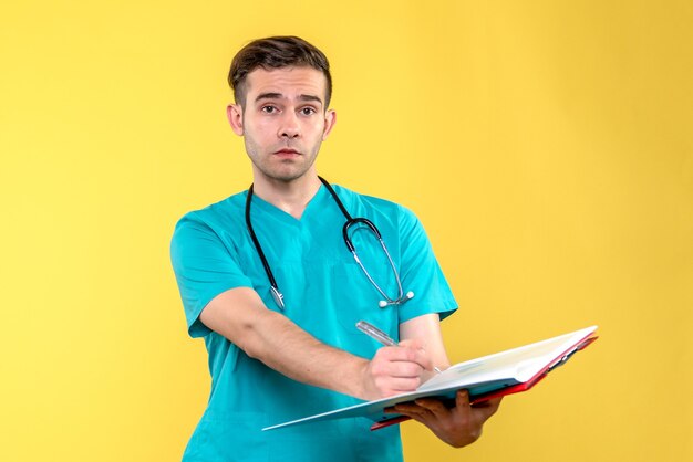 Vista frontal del joven médico sosteniendo análisis sobre pared amarilla