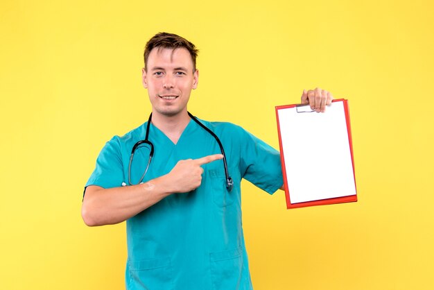 Vista frontal del joven médico sosteniendo análisis sobre pared amarilla