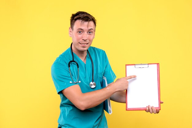 Vista frontal del joven médico sosteniendo análisis sobre pared amarilla