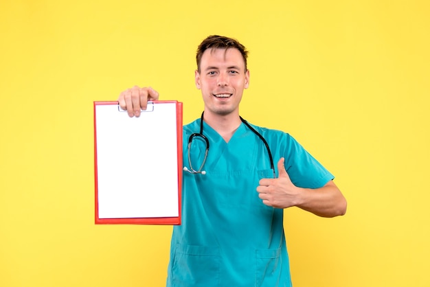 Vista frontal del joven médico sosteniendo análisis sobre pared amarilla