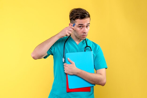 Vista frontal del joven médico sosteniendo análisis sobre pared amarilla