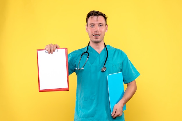 Vista frontal del joven médico sosteniendo análisis sobre pared amarilla