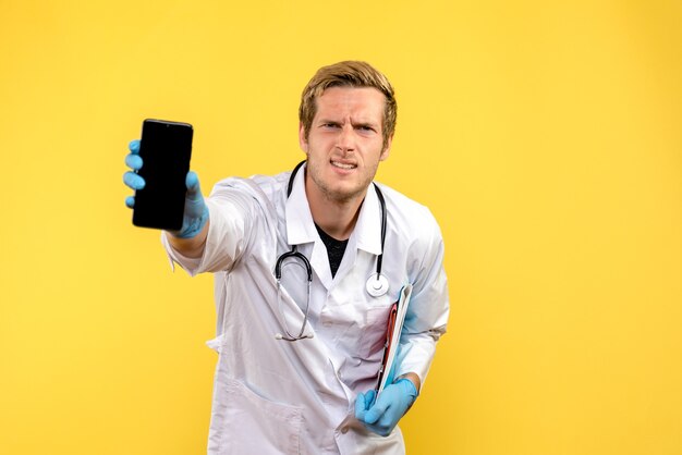 Vista frontal joven médico sosteniendo el teléfono en el escritorio amarillo médico de salud virus humano