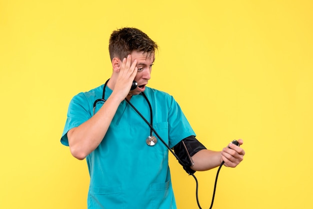 Vista frontal del joven médico con tonómetro en la pared amarilla