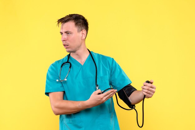 Vista frontal del joven médico con tonómetro en la pared amarilla