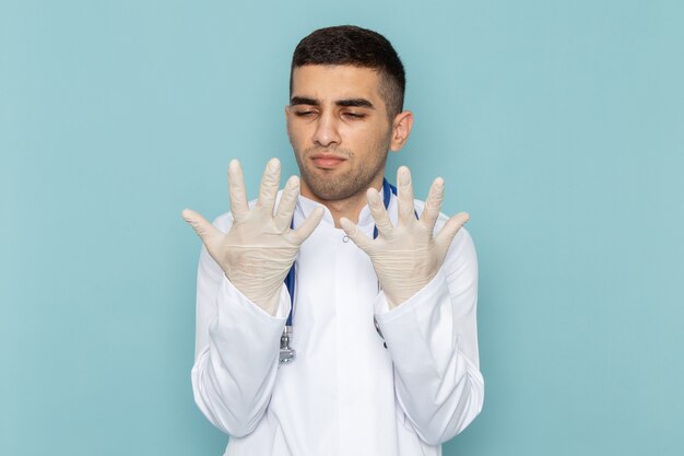 Vista frontal del joven médico en traje blanco con estetoscopio azul comprobando sus manos