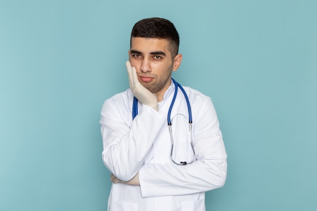 Vista frontal del joven médico en traje blanco con estetoscopio azul con expresión deprimida