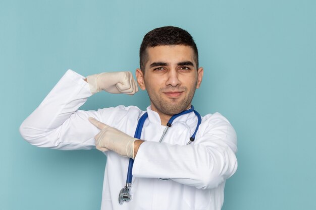 Vista frontal del joven médico en traje blanco con estetoscopio azul flexionando