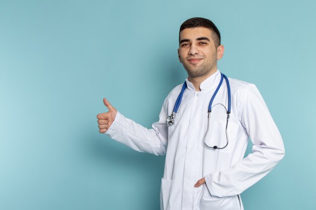 Vista frontal del joven médico en traje blanco con estetoscopio azul posando