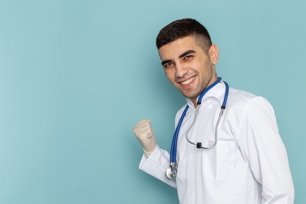 Vista frontal del joven médico en traje blanco con estetoscopio azul sonriendo