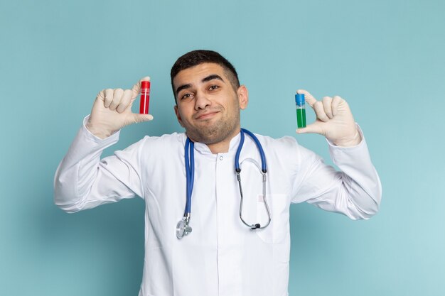 Vista frontal del joven médico en traje blanco con estetoscopio azul sosteniendo frascos