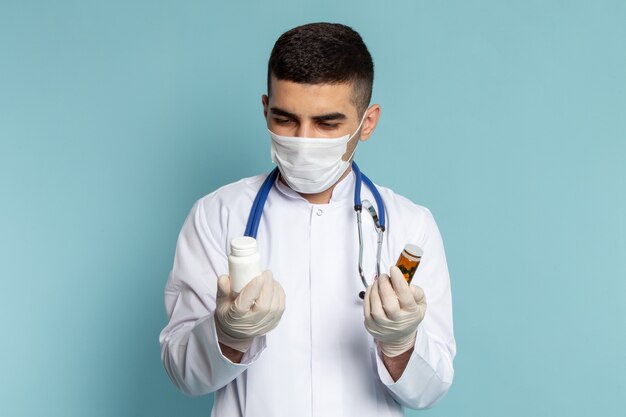 Vista frontal del joven médico en traje blanco con estetoscopio azul sosteniendo pastillas